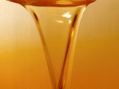 Gold syrup like liquid is being poured into a glass bowl.