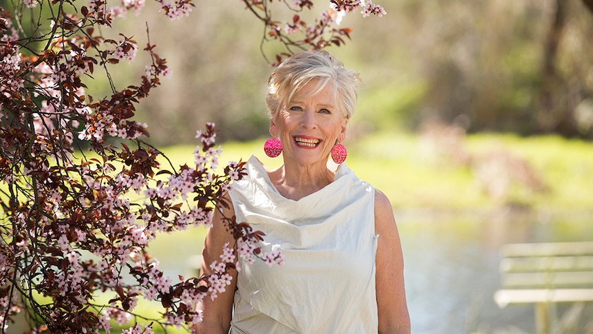 Maggie Beer standing next to a flowering tree with pale pink blossoms.