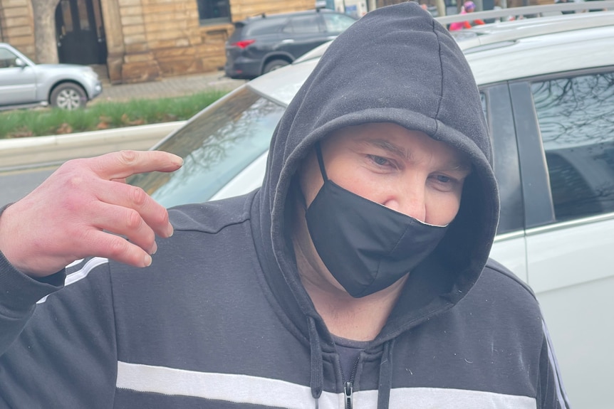 A man wearing a black mask and dark jumper with a hood 