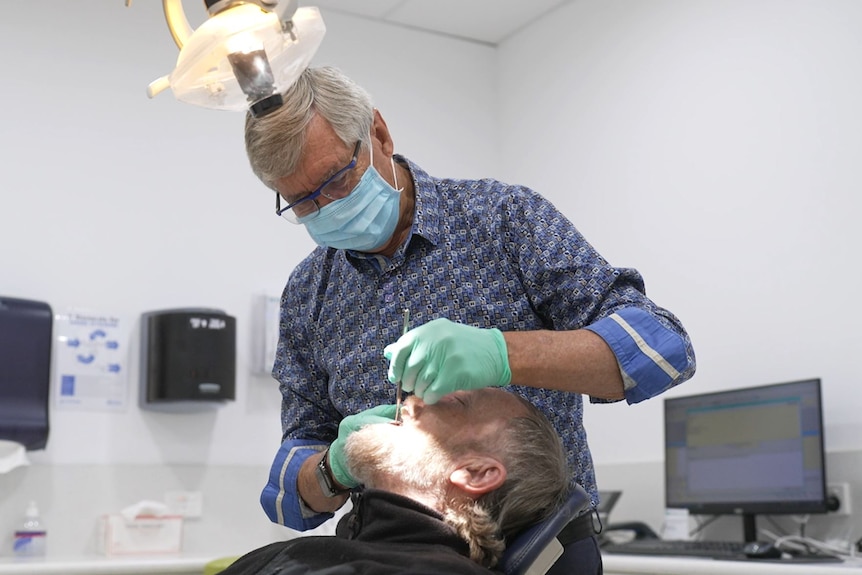 a dentist working on a mans teeth under bright lights 