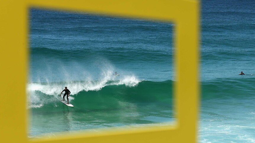 A surfer is seen through the sculpture 'Time Frame' being displayed at the Sculpture by the Sea exhibition