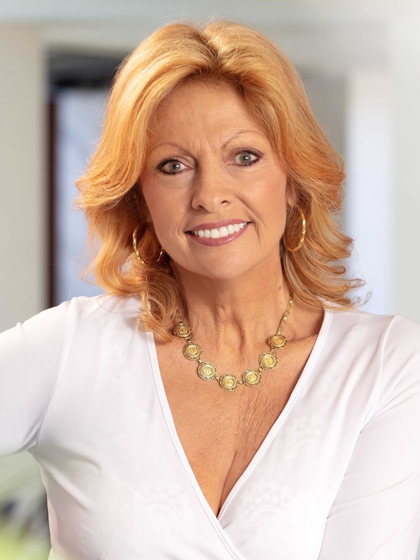 A woman with shoulder-length blond hair, a white top and hoop earrings smiling