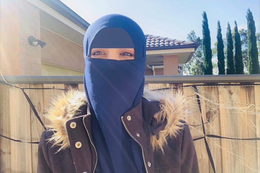 A woman wearing jacket outside standing in front of a fence