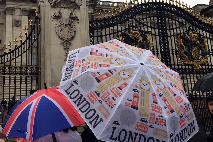 People hold London-themed umbrellas at the gates of Buckingham Palace.