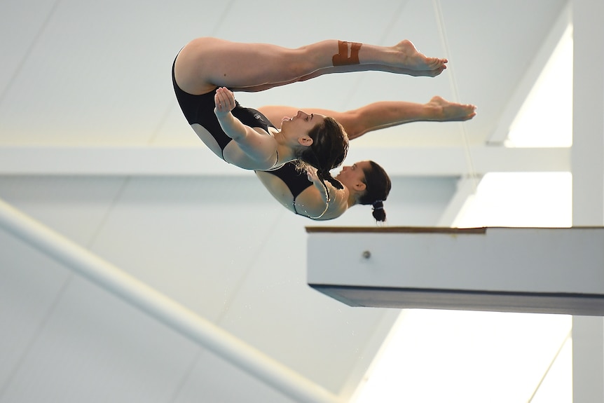 Two female divers in action, their legs are horizontal and their arms outstretched 