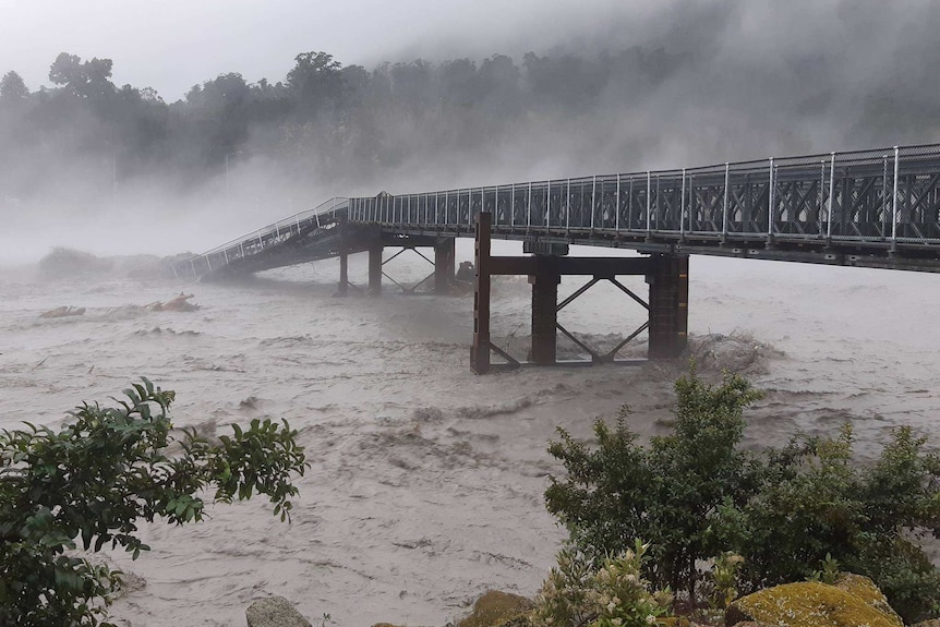 A bridge is seen half-collapsed on the far side in a rampaging river as rain falls during a storm