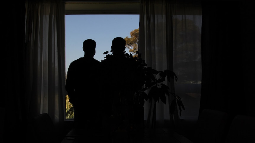 Silhouette of two men in their living room in front of a window