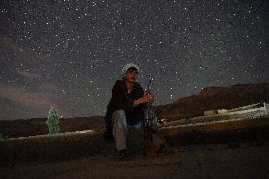 Against a starry sky, a fighter sits with his rifle ready. 