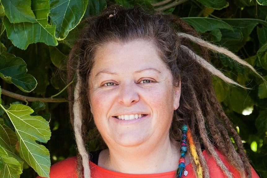 A woman in a red shirt with dreadlocks smiles at the camera