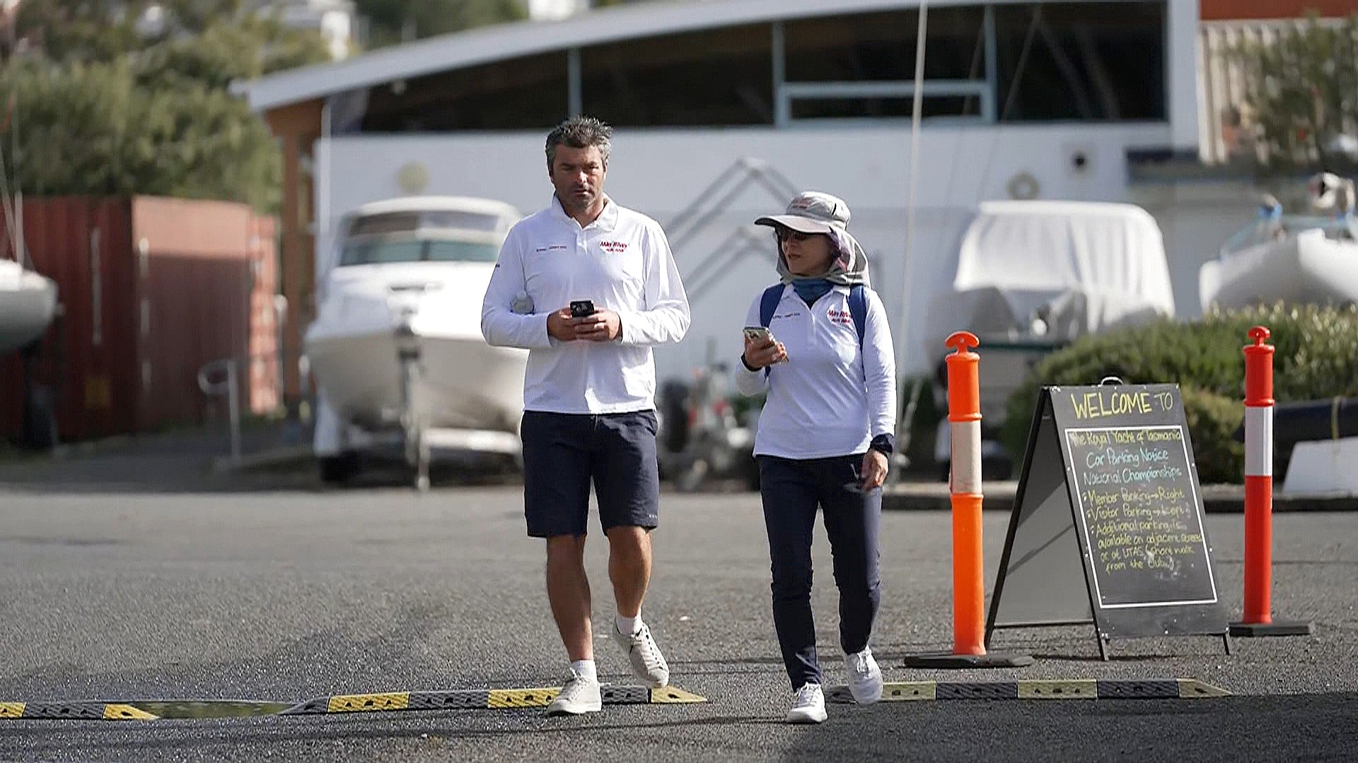 Un hombre y una mujer con camisetas blancas caminan por un estacionamiento.