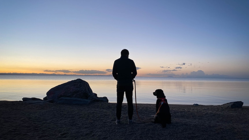 Man and dog silhouetted in the sunset by a lake