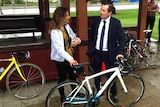 Mark McGowan stands next to a woman holding a bike helmet with both of them holding a white bicycle.