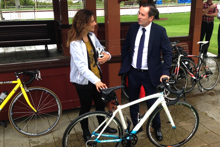 Mark McGowan stands next to a woman holding a bike helmet with both of them holding a white bicycle.