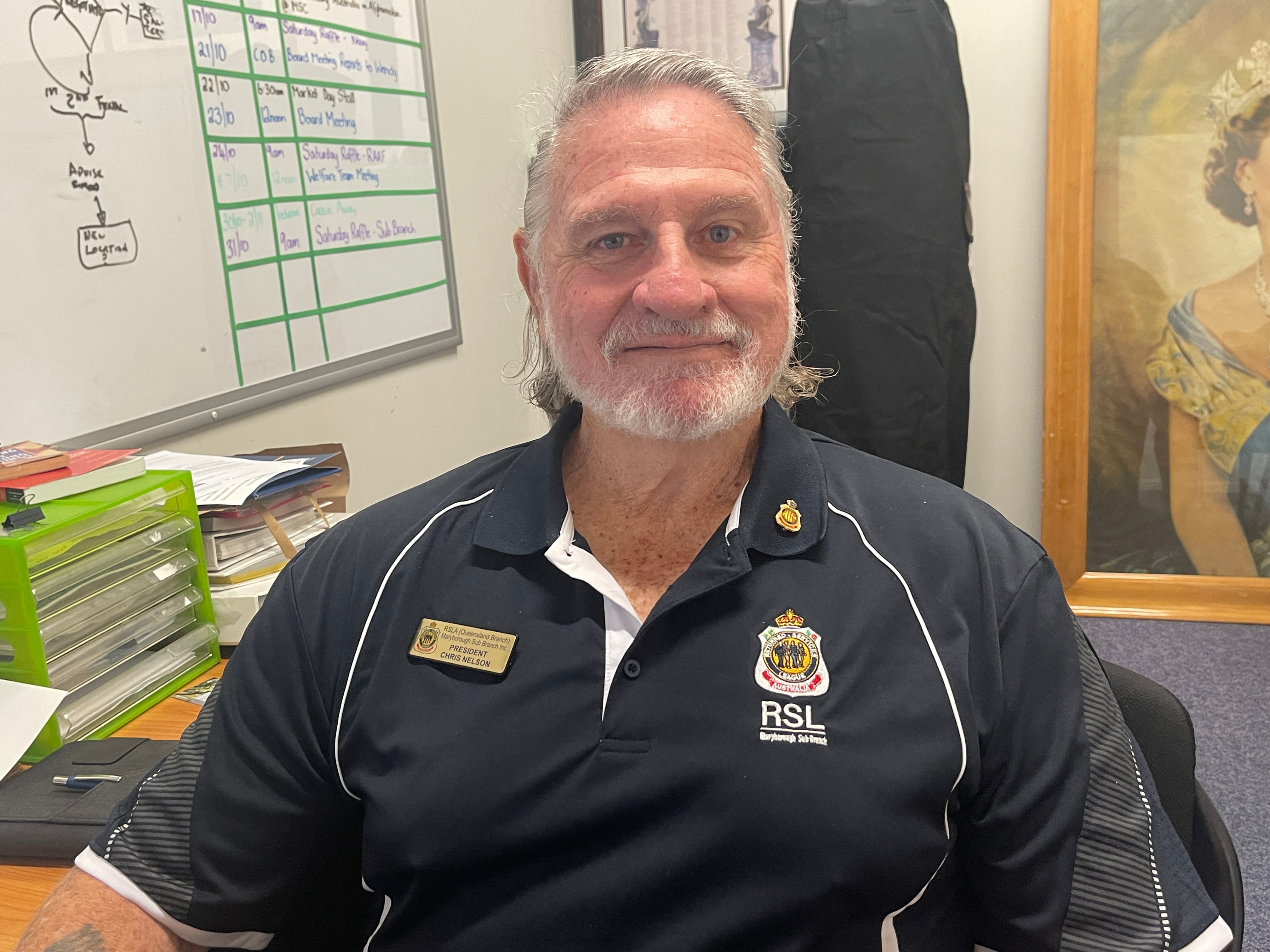An older man with a dark blue polo shirt smiles fondly in his RSL sub-branch uniform.