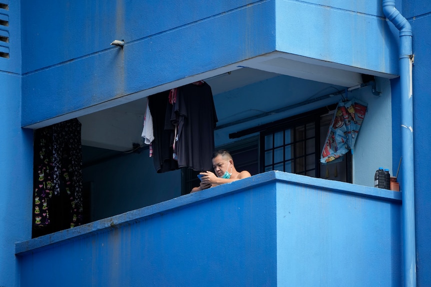 A man reads from his mobile phone outside on the balcony of his apartment 