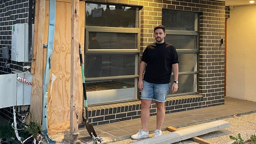 man in black t-shirt and denim shorts standing on verandah of home being renovated