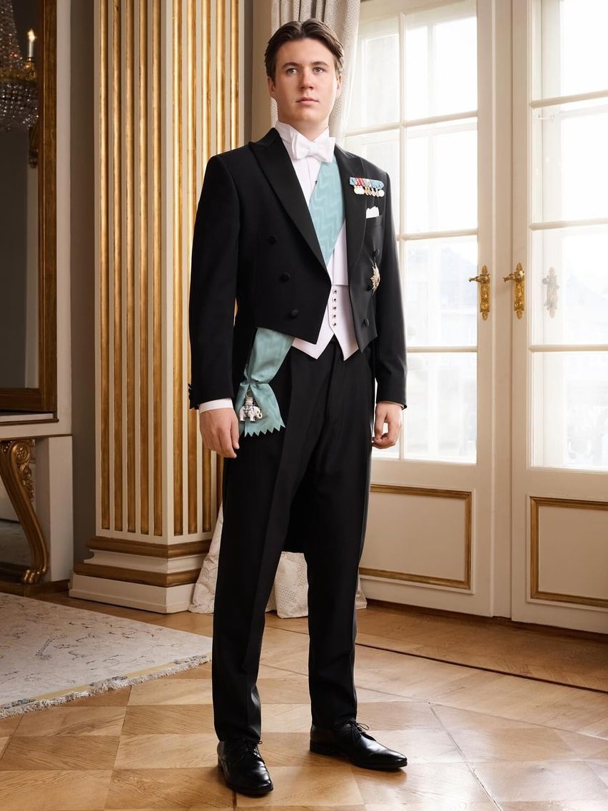 Prince Christian in a suit and sash standing in a polished white room