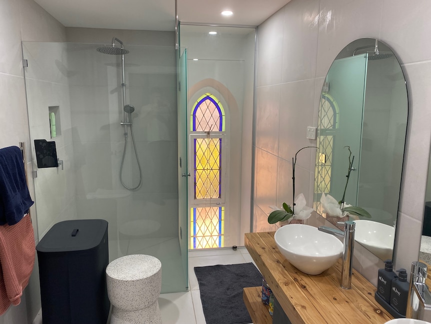 A bathroom with a shower, sink and stained window. 