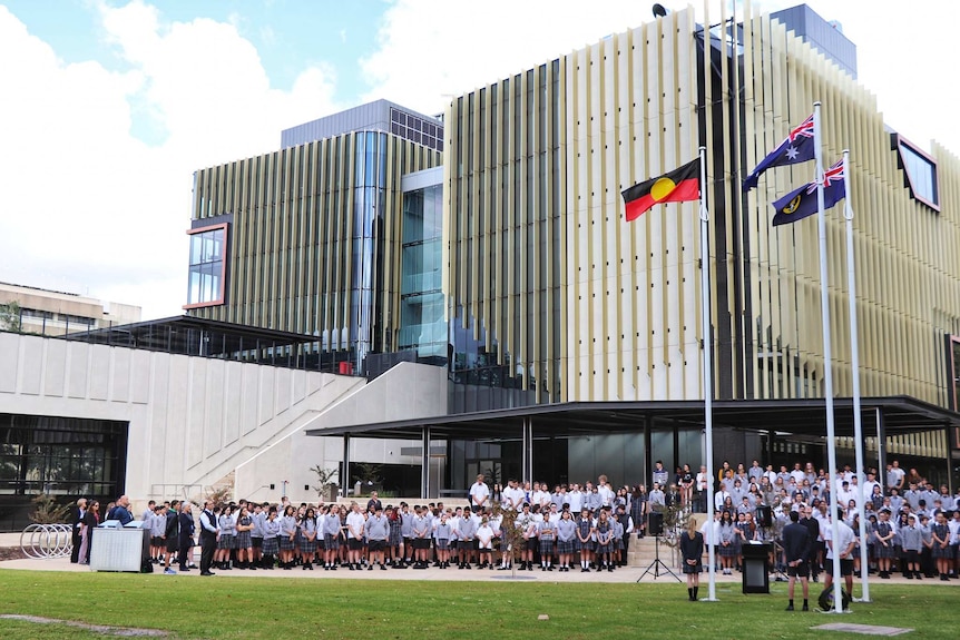 Large multi-storey, inner city building with school students and staff gathered on the lawn out the front.