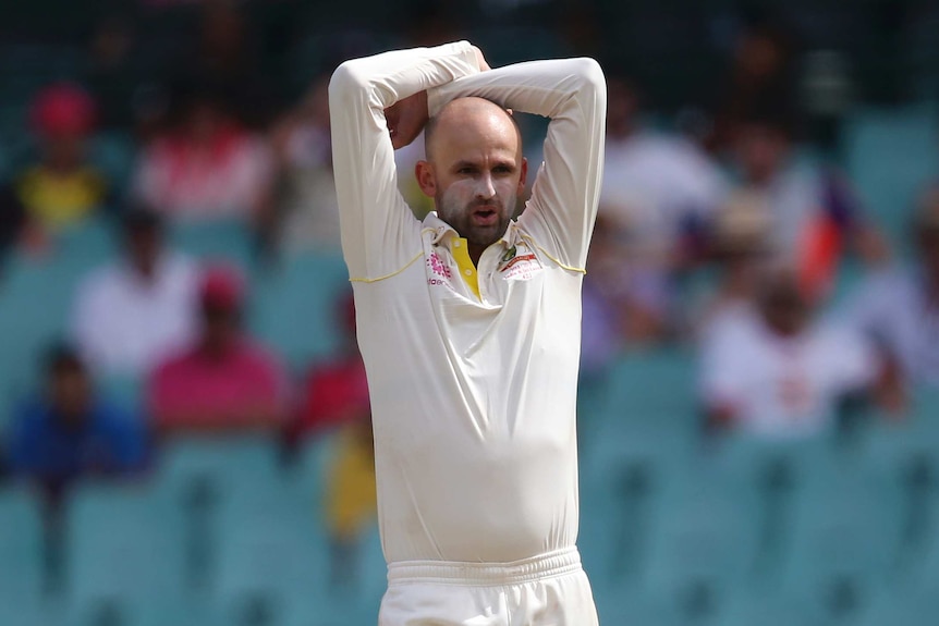 Australia bowler Nathan Lyon, wearing sunscreen on his nose and cheeks, stands with his arms over his head during a Test match.