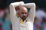 Australia bowler Nathan Lyon, wearing sunscreen on his nose and cheeks, stands with his arms over his head during a Test match.