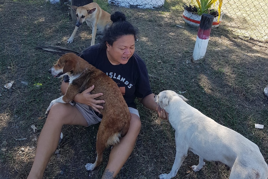 A woman sits on the ground surrounded by three dogs. 