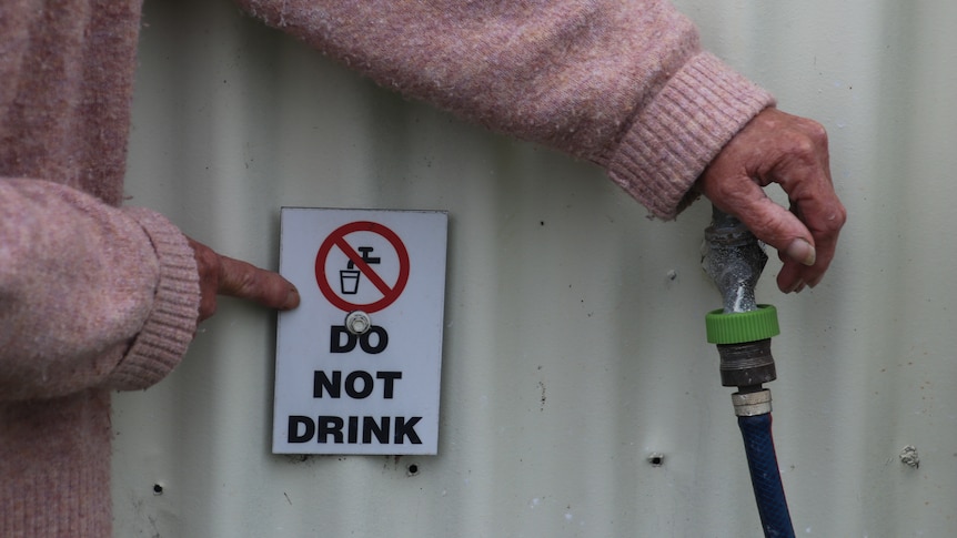 A woman pointing to a host tap and a sign reading "do not drink".