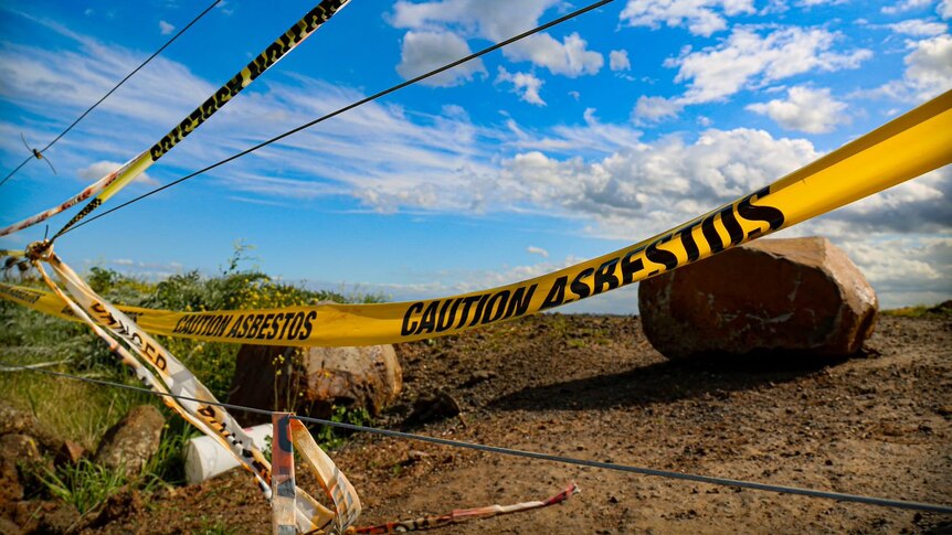 A yellow warning sign is draped across a fence in front of rocks and soil
