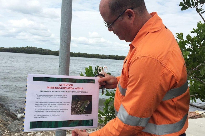 An environment officer erects a sign warning fishers on the Brisbane River.