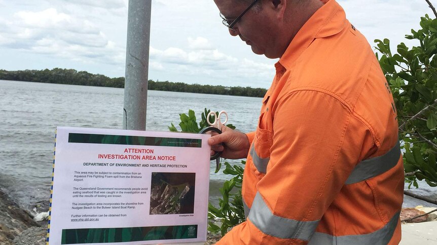 An environment officer erects a sign warning fishers on the Brisbane River.