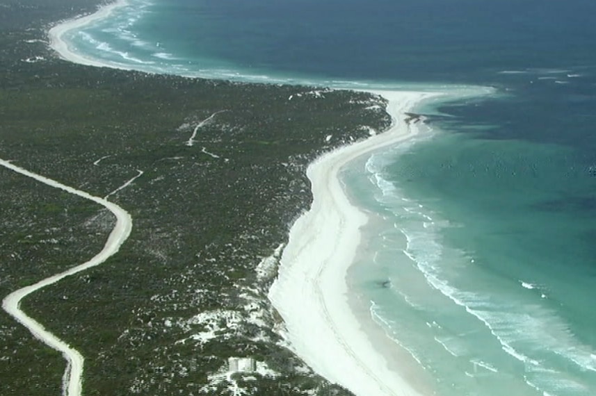 An aerial shot of a stretch of WA coastline with sand dunes and shrubland on one side and blue ocean on the other.