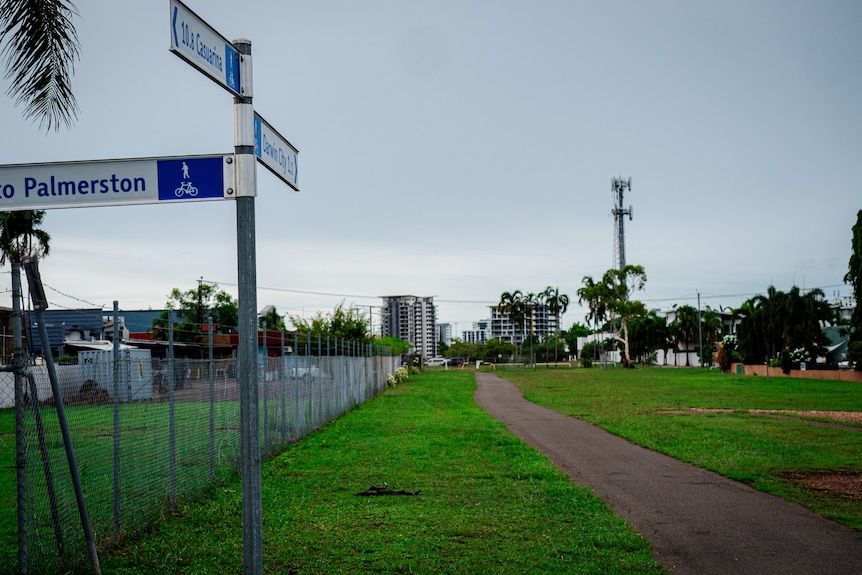 a cycle path through a grassy area with signposts and a steel fence.