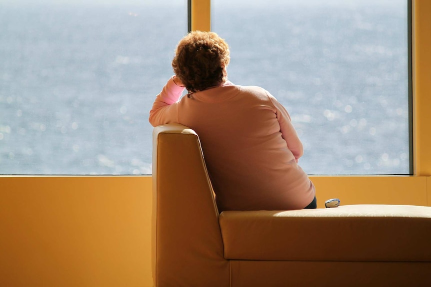 Older woman sits alone looking out window.