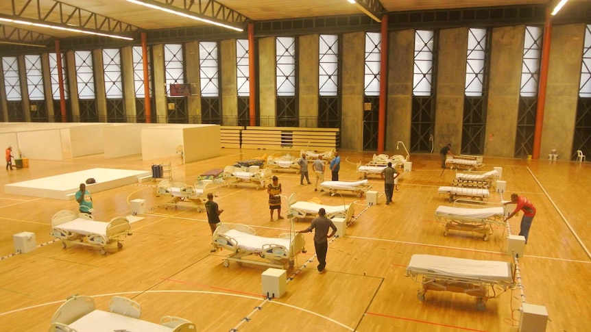 People stand in a large room setting up hospital beds.