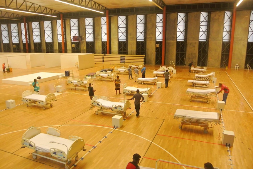 People stand in a large room setting up hospital beds.