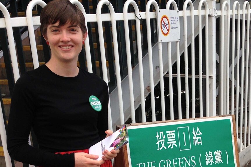 A woman stands next to a Greens sign.