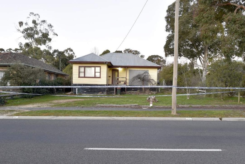 A cream coloured weatherboard house with police tape around it.