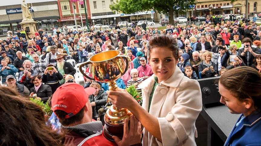 Michelle Payne, on an outdoor stage, holds the Melbourne Cup for the crowd to see in Ballarat.