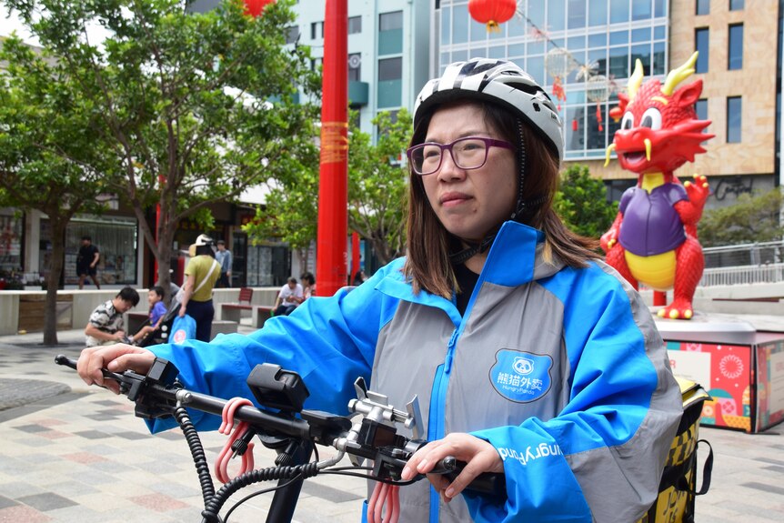 A woman stands holding the handle bars of a food delivery bike.