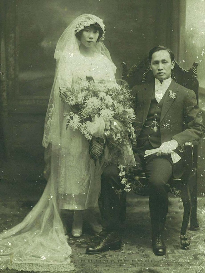 An old black and white photograph of a chinese couple in western style wedding dress.