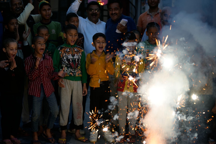 Children clap and cheer as fireworks explode in front of them. 