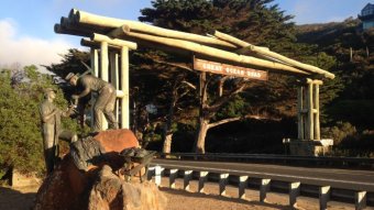A bronze statue of two men cutting rocks with a pick stands beside the Great Ocean Road timber memorial arch