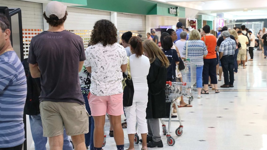 A long line of shoppers queues outside a Woolworths store inside a shopping centre.