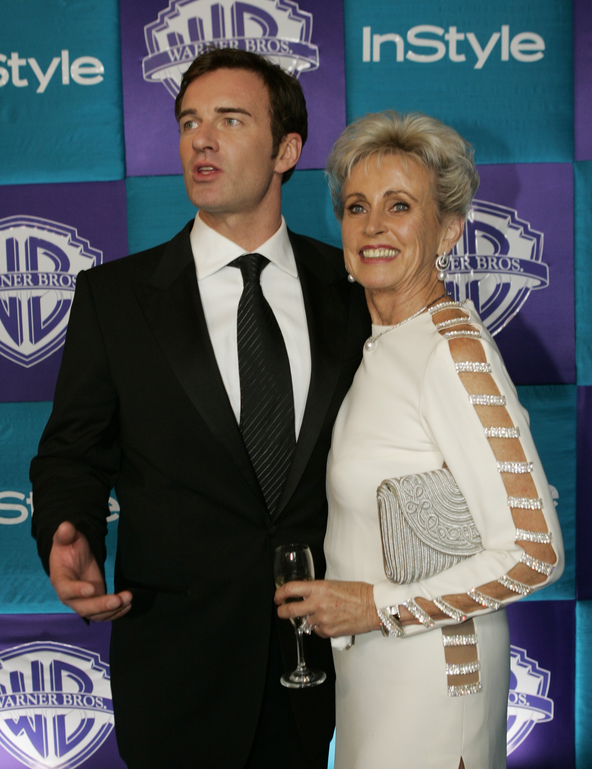 Julian McMahon wears a suit while Lady Sonia McMahon wears a white long sleeved dress with cutouts up the arm and sides
