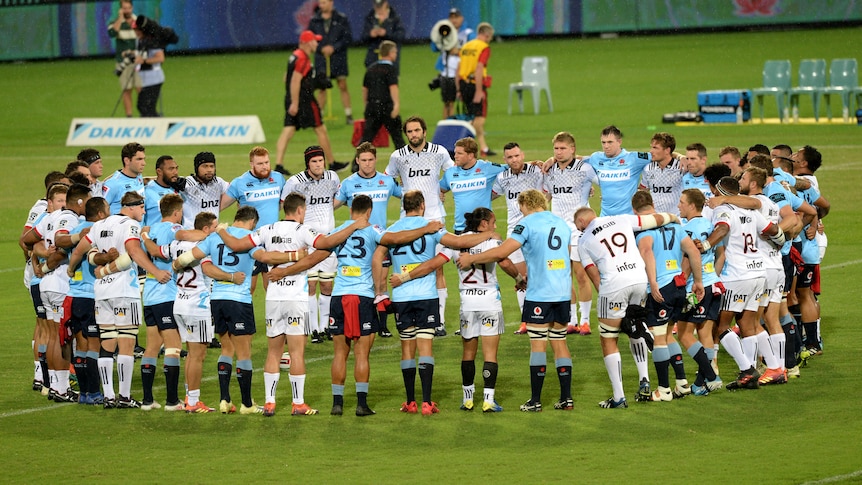 Waratahs and Crusadersplayers huddle in a ring for minute's silence before the start of play in a Super Rugby match