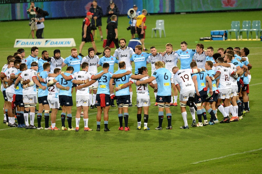 Waratahs and Crusaders players huddle in a ring for minute's silence before the start of play in a Super Rugby match