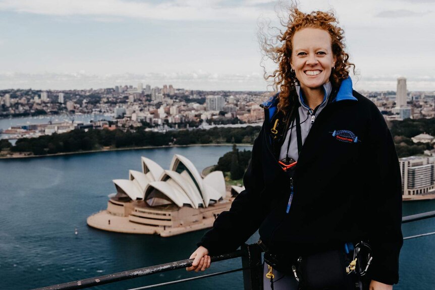 BridgeClimb operations coordinator Ashleigh Millet stands atop the Sydney Harbour Bridge with the Opera House below.