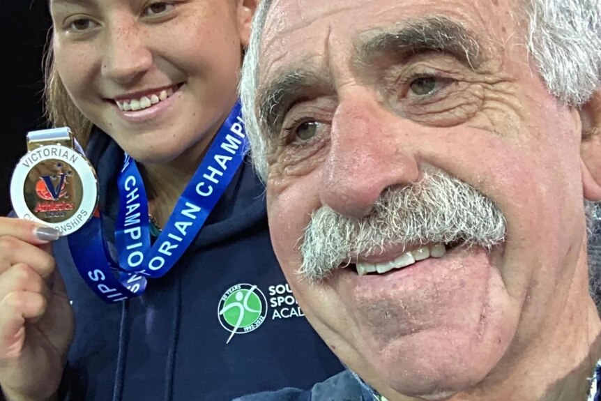 a teenage girl in a selfie with a medal, next to her dad 