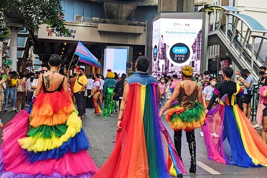 the back of a group of four people dressed in bright rainbow colours walking down the street