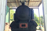 A small locomotive under a shed on a rural property.